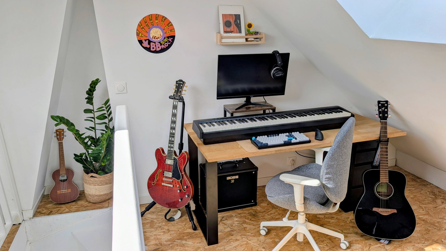 Un coin sous les toits avec un bureau, un piano numérique, une guitare électrique, une acoustique, un ukulélé et un petit ampli