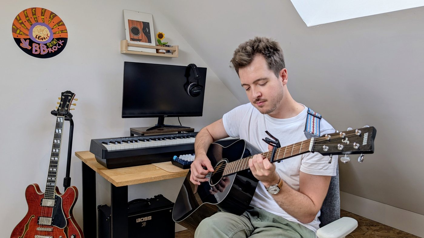 Pierre joue en fingerstyle sur une guitare acoustique noire avec un capodastre